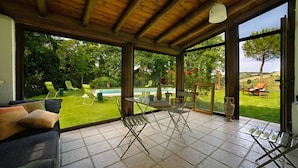 A spacious patio with a glass table and chairs, a sofa, and a view of a lush garden and pool. - Luce tra i Faggi 8 in Montemaggiore al Metauro (Colli al Metauro)