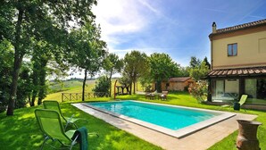 A rectangular swimming pool with a tiled deck, surrounded by lush green grass and trees. - Luce tra i Faggi 8 in Montemaggiore al Metauro (Colli al Metauro)