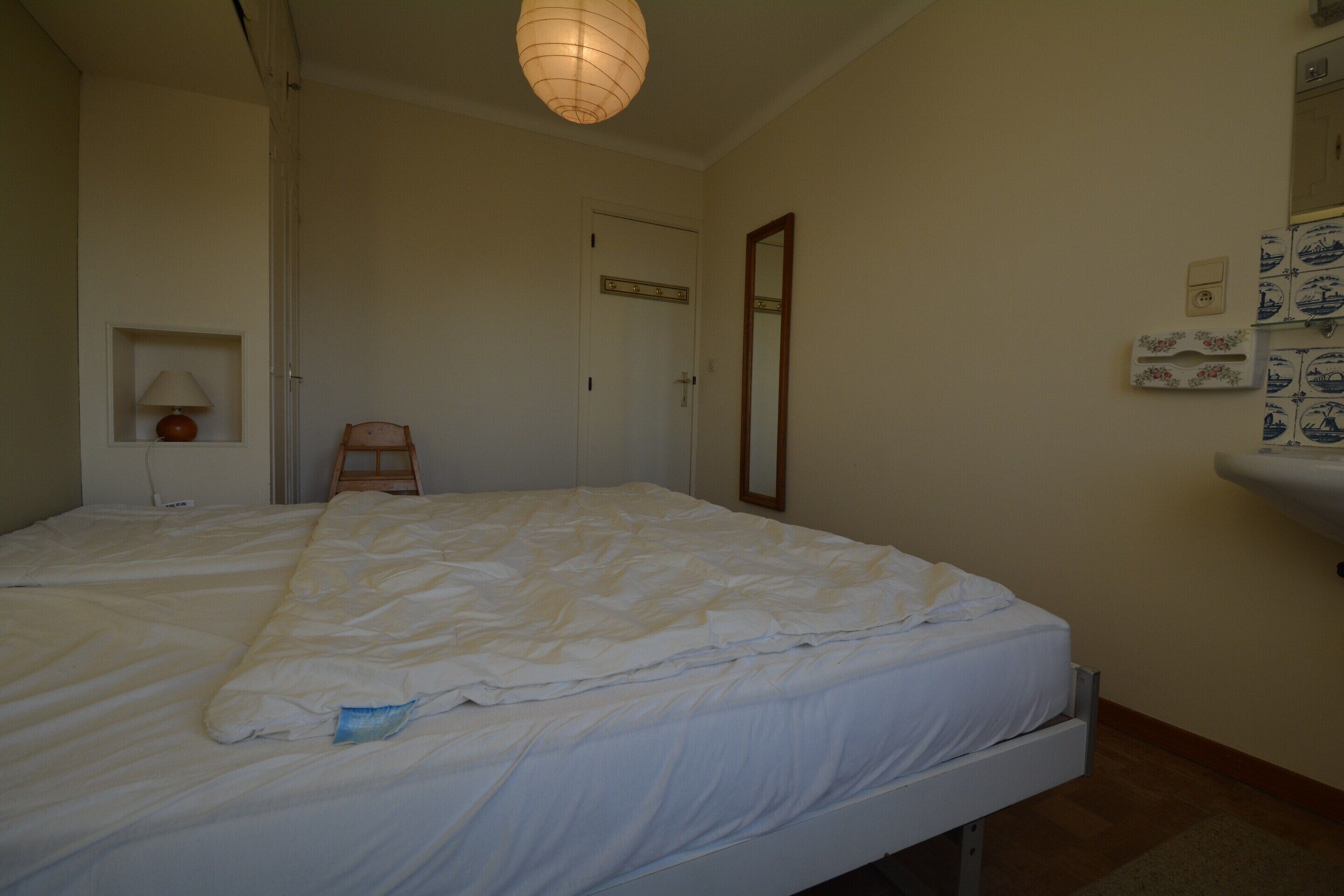 Une chambre à coucher avec un lit, une table de chevet, une lampe, un miroir et une porte.