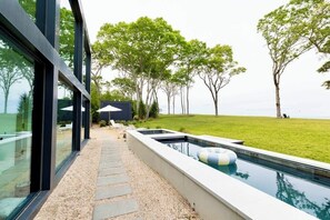 A modern outdoor pool area with a stone pathway, a lounge chair, and a view of the sea.