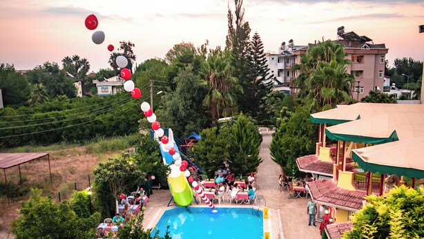 A pool area with a slide, surrounded by greenery and buildings. - MARİN HOTEL (Kemer)