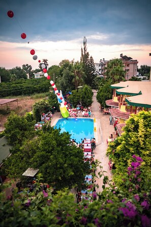 Uma área de piscina com um escorregador, rodeada por vegetação e edifícios.