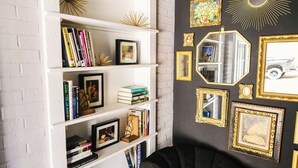 A room with a white brick wall, a black upholstered chair, and a white bookshelf with various items. - The Overlook on Chocolate (Hershey)