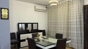 Un coin repas comprenant une table avec un plateau en verre, quatre chaises, un meuble noir et blanc et un luminaire suspendu.