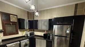 Une cuisine compacte équipée d’appareils électroménagers en acier inoxydable, d’un lave-linge, d’un four à micro-ondes et d’un réfrigérateur. On y trouve un petit tabouret rose et une chaise blanche.