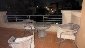 Un balcon agrémenté de meubles en osier et d’une table en verre, offrant une vue sur le paysage urbain illuminé la nuit.