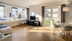 A modern living room with a large window, a flat-screen TV, a dining area with chairs, and a radiator under the window. - Apartment by the Seawall in Belgium (Knokke-Heist)