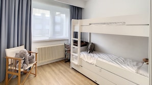A bunk bed room with a wooden chair, a radiator, and a window with curtains. - Apartment by the Seawall in Belgium (Knokke-Heist)