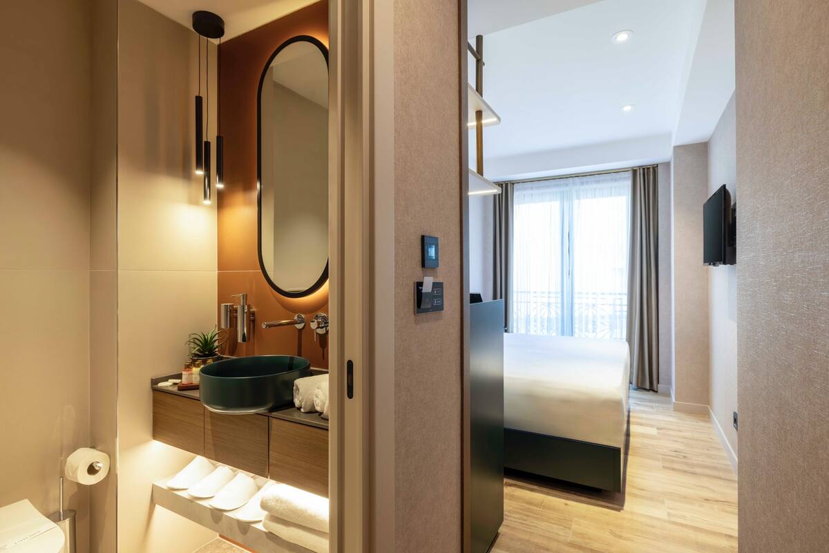 A modern hotel bathroom with a large mirror, a sink, and a toilet.