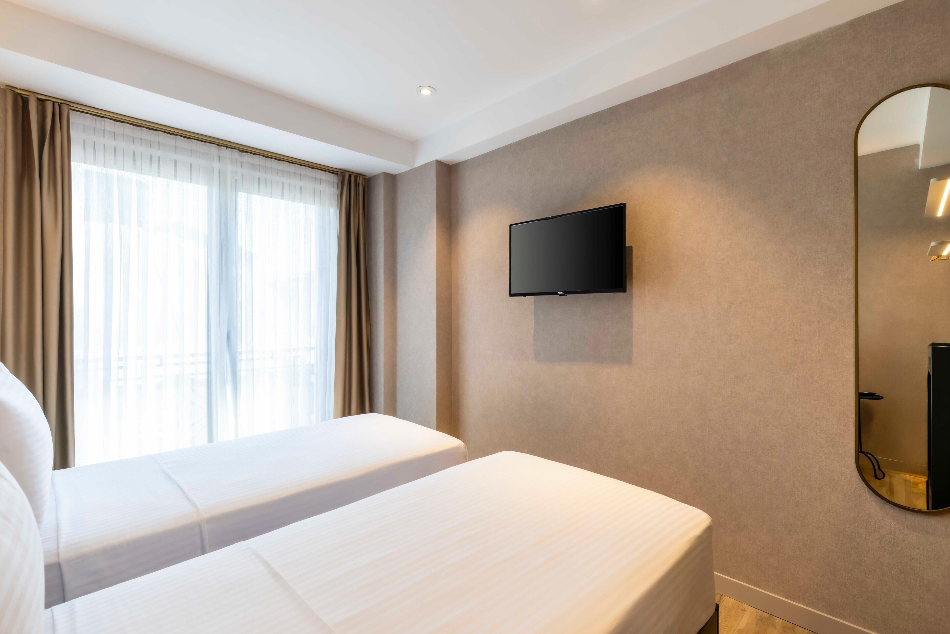 A hotel room with two beds, a flat-screen TV mounted on the wall, and a large mirror.