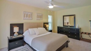 Une chambre à coucher comprenant un lit, des tables de chevet, une commode, un ventilateur de plafond et des œuvres d’art murales.