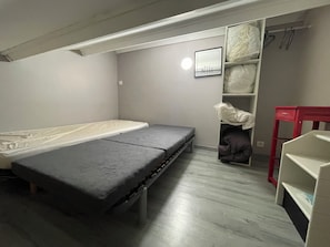 Une petite piĂšce, de taille modeste, comprenant un lit, une table rouge et une armoire oĂč sont suspendus des vĂȘtements.