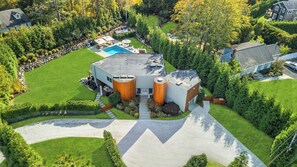 An aerial view of a modern house with a swimming pool, a garage, and a well-maintained lawn. - Modern, resort-style retreat in the heart of Shinnecock Hills, luxurious... (Southampton)