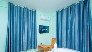 Una habitación de hotel con cama, una silla de madera, televisor y cortinas.
