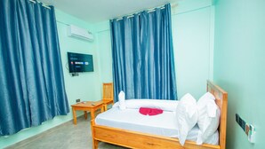 Habitación de hotel con cama de madera, una pequeña mesa de madera, una silla, televisor montado en la pared y teléfono también en la pared.