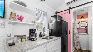 A compact kitchen with white cabinets, a black refrigerator, a coffee maker, and a window with blinds.