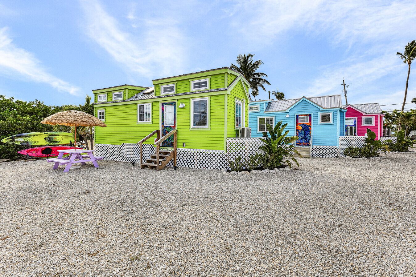 Une propriété colorée située en bord de mer, avec une maison verte, une maison bleue et une maison rose, chacune étant entourée d’une clôture blanche en bois.