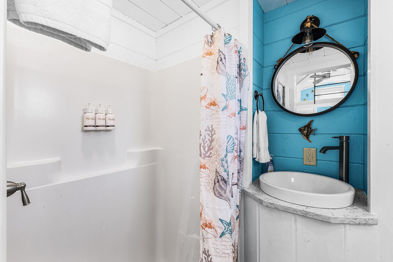 Een badkamer met een wit bad, een blauwe accentmuur, een ronde spiegel en een witte wastafel.