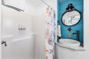 A bathroom with a white bathtub, a blue accent wall, a round mirror, and a white sink. - Matlacha Tiny Village - Dolphin (Matlacha)