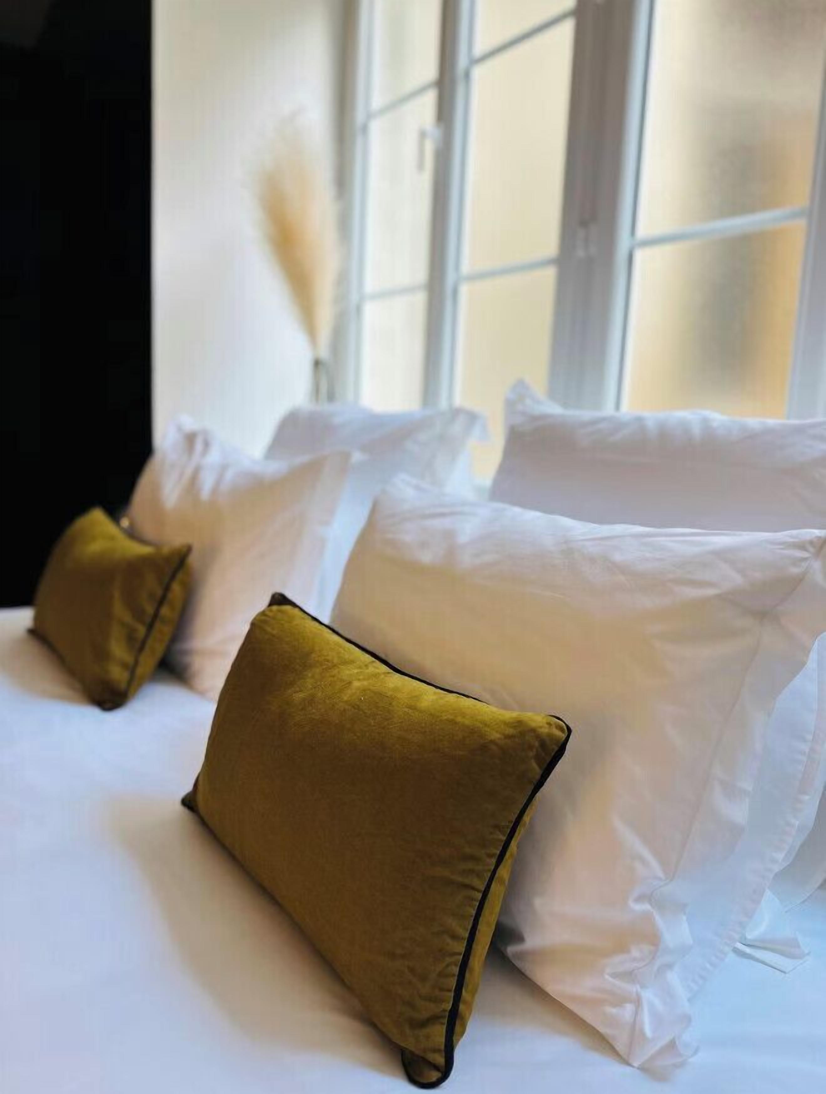 A hotel room with a bed featuring white pillows and a single mustard-colored pillow.