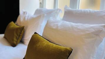 A hotel room with a bed featuring white pillows and a single mustard-colored pillow.