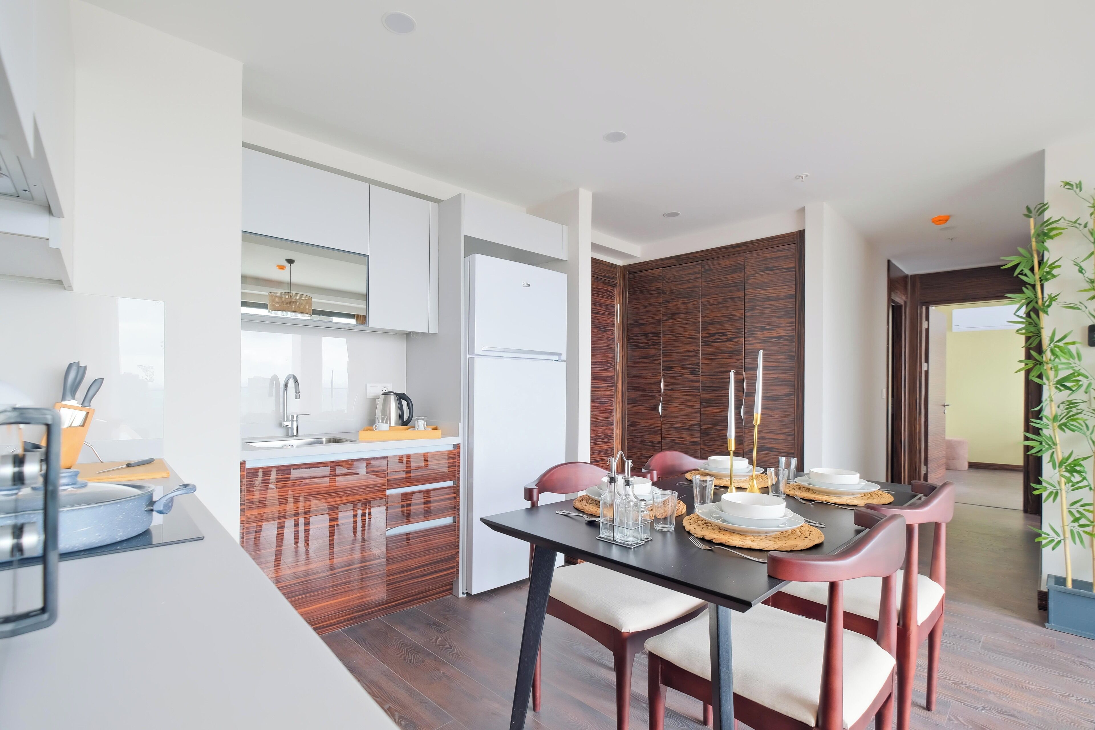 Een moderne keuken met witte kasten, een houten eethoek met een tafel gedekt voor vier personen, en een uitzicht op de aangrenzende kamer.