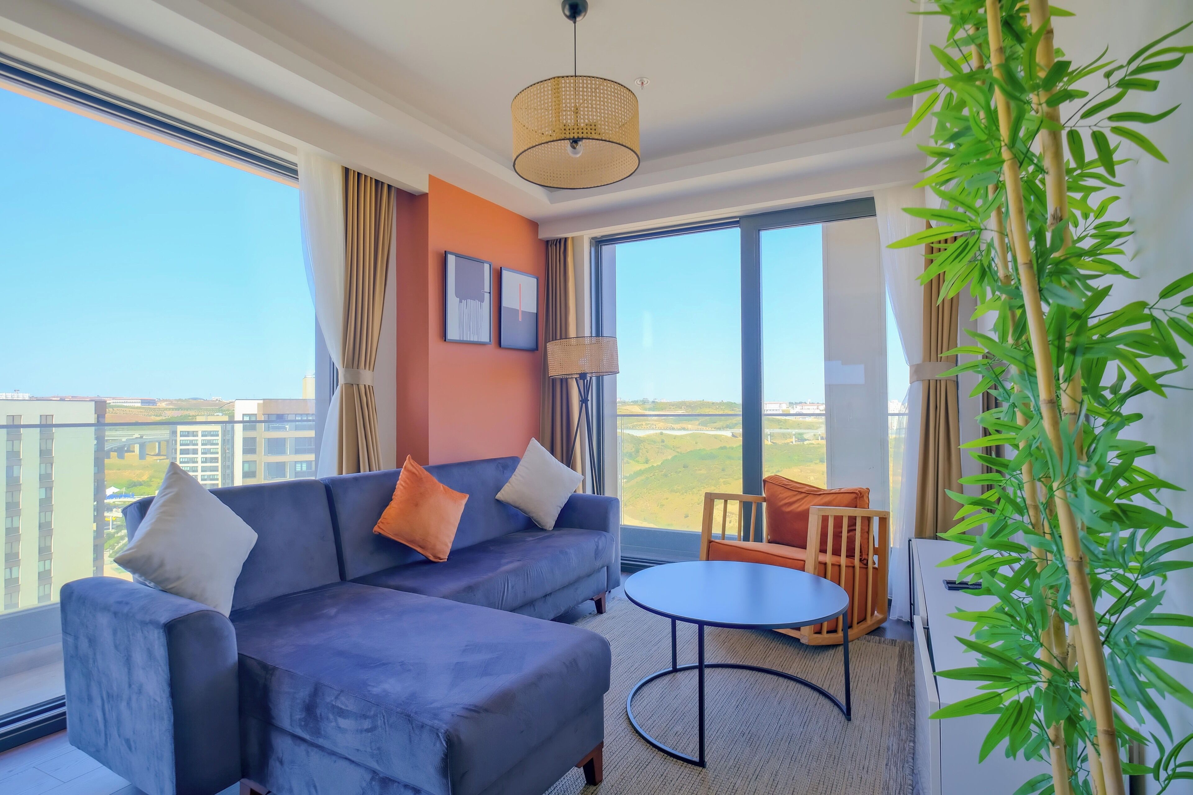 A modern living room with a sofa, a round table, and a large window offering a view of the cityscape.