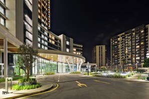 Un edificio moderno con fachada de vidrio curvada y un área ajardinada con un árbol y plantas.