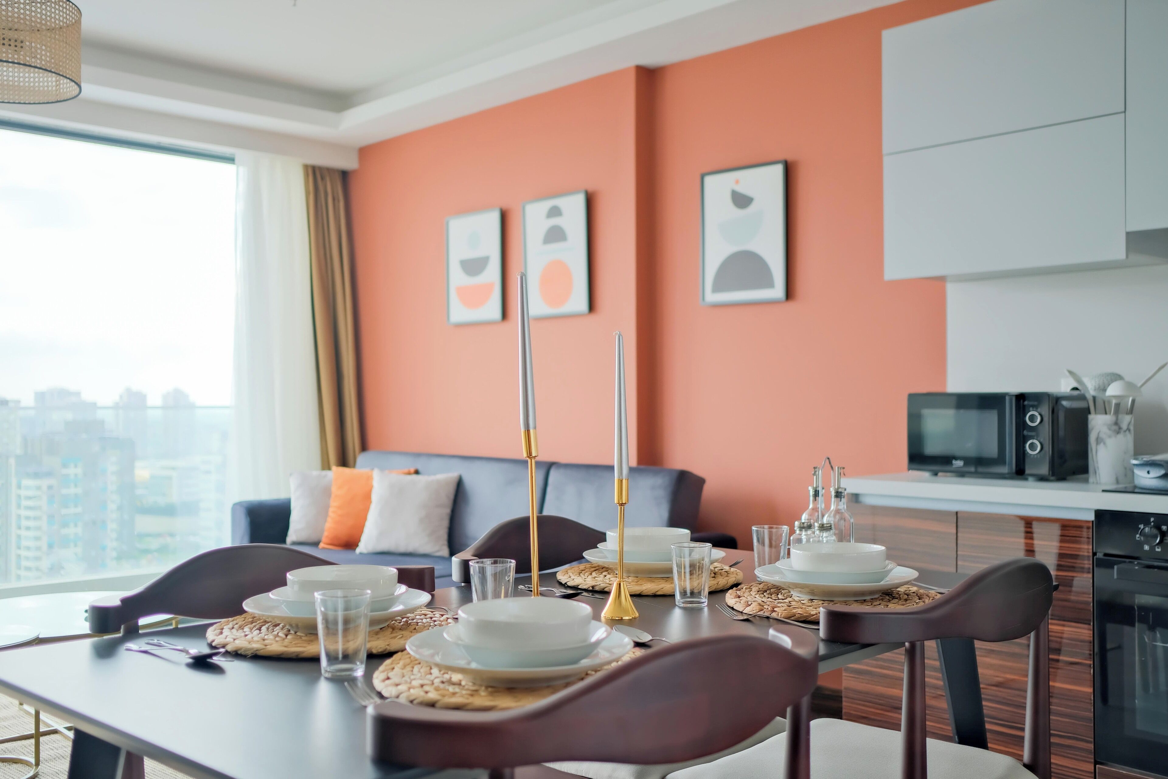A dining area with a table set for four, a sofa in the background, and a kitchen area visible to the right.