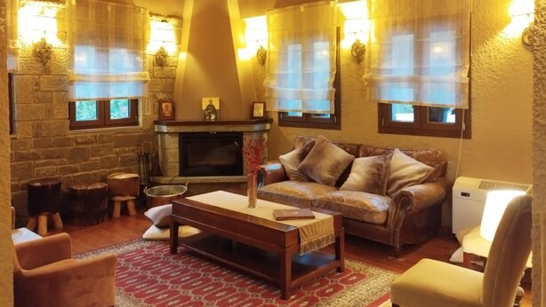 A cozy living room with a fireplace, leather sofa, wooden coffee table, and a red patterned rug. - Agathi Hotel  (Central Tzoumerka)