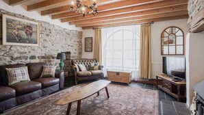 A cozy living room with a stone wall, a wooden ceiling, a leather sofa, a wooden coffee table, and a television. - Coach House (Llandysul)