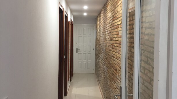 Un couloir avec une porte blanche au fond, un mur de briques d’un côté et un mur blanc de l’autre.