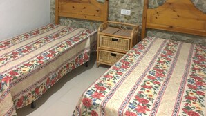 Une chambre avec deux lits simples, une petite table en bois et un mur en pierre.