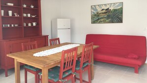 Un coin repas avec une table en bois, des chaises rouges, un canapé rouge et un réfrigérateur blanc.