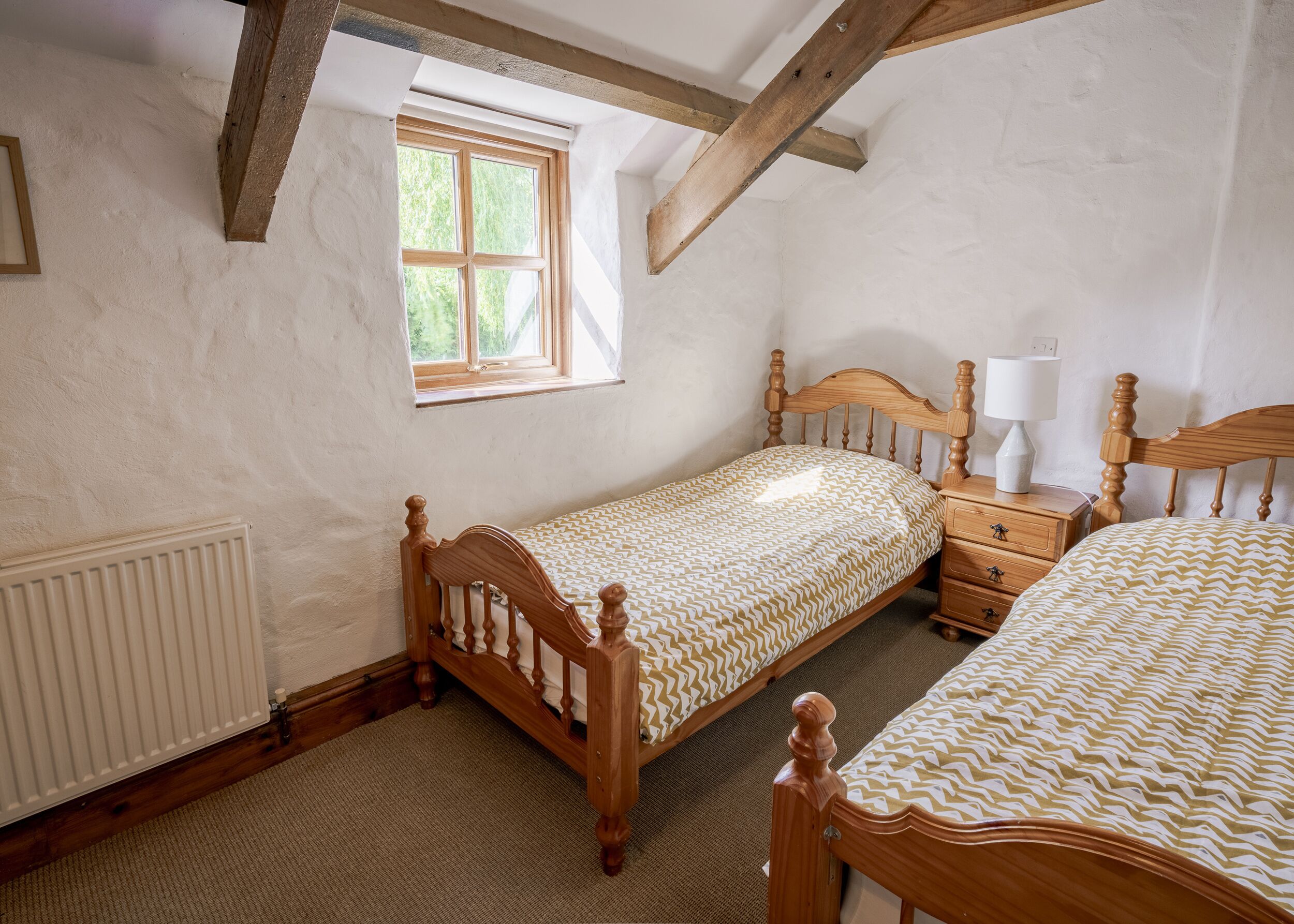 A bedroom with two wooden beds, a window, a radiator, and a nightstand with a lamp.