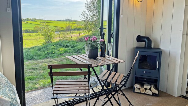 Un espace extérieur accueillant, aménagé avec une table et des chaises, un poêle à bois et offrant une vue pittoresque sur des champs verdoyants.