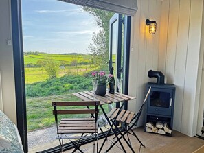 Ein gemütlicher Sitzbereich im Freien mit Tisch und Stühlen, einem Kaminofen und einem herrlichen Blick auf grüne Felder.