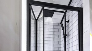 Une salle de bain moderne avec une cloison en verre, des murs recouverts de carreaux blancs et un cadre noir.