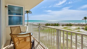 A balcony with wicker chairs, a table, and a view of the beach and ocean. - Estero Beach & Tennis 207-a (Fort Myers Beach)