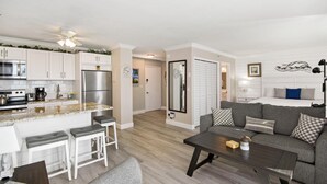 A modern apartment with a kitchen, dining area, and living room. It includes a refrigerator, stove, and bar stools. - Estero Beach & Tennis 207-a (Fort Myers Beach)