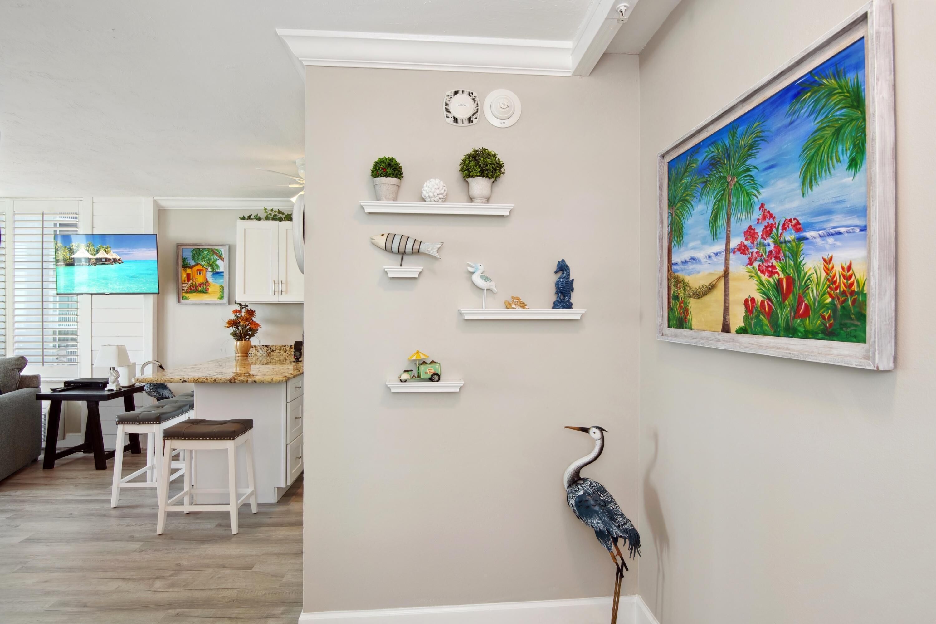 A modern kitchen with white cabinetry, a dining area with a gray sofa, and a painting of a tropical scene.