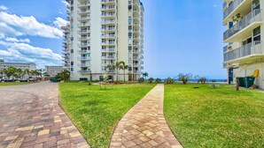 A multi-story hotel with a paved walkway and grassy areas, overlooking a body of water. - Estero Beach & Tennis 207-a (Fort Myers Beach)