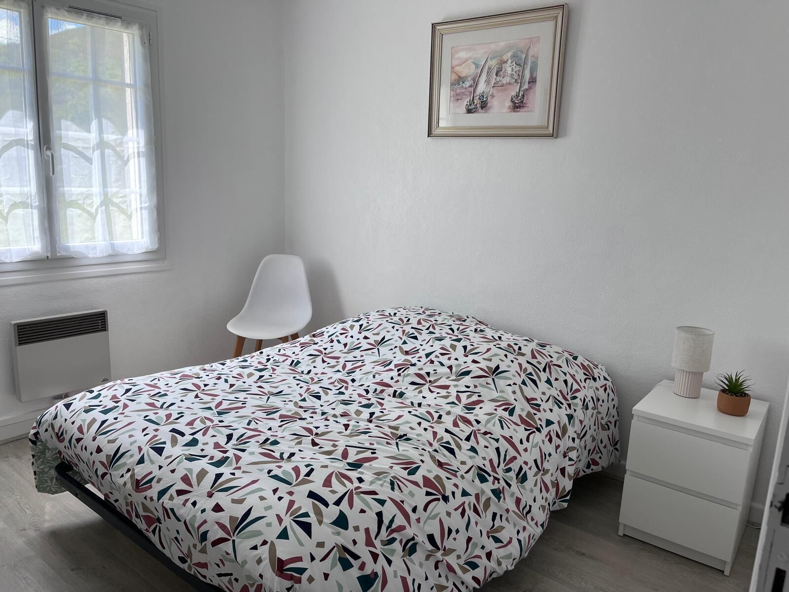 Une chambre à coucher avec un lit, une chaise, une table de chevet avec une lampe et un tableau encadré au mur.