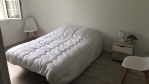Et soveværelse med seng, stol, natbord, lampe og et billede i ramme på væggen.