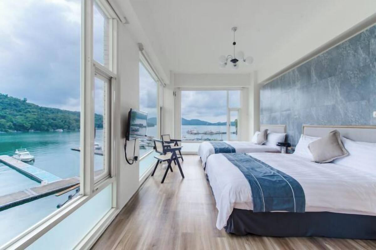 A bedroom with a large window, a bed, a desk, and a chair.