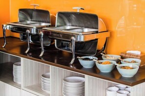 Montaje de bufé con dos dispensadores de comida caliente, tazones de cereal y platos apilados.