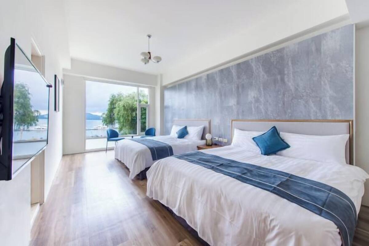 A hotel room with two beds, a large window, and a view of the outdoors.
