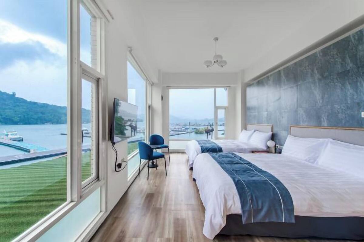 A hotel room with two beds, a TV, a chair, and a view of a body of water.