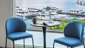 A room with two blue chairs, a small round table with a newspaper and a mug, and a view of a marina with boats. - Shui Yang Lakeview House with Elevator (Nantou)