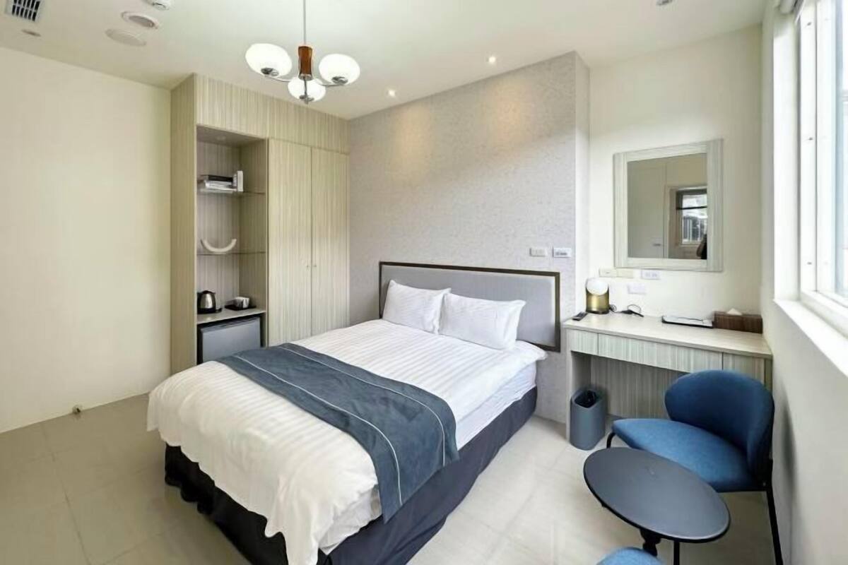 A modern bedroom with a bed, bedside tables, a desk, a chair, and a mirror.
